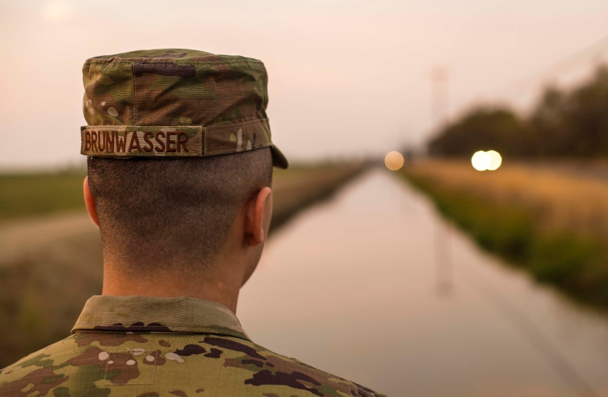 A man in a military uniform looks out on an irrigation canal running adjacent to a highway.