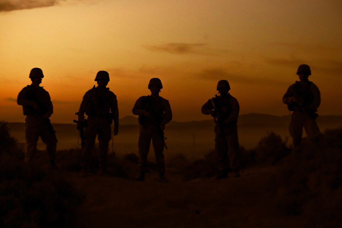 Five Marines are silhouetted against an orange sky.