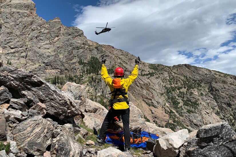 A helicopter flies over a mountain as a person watches.