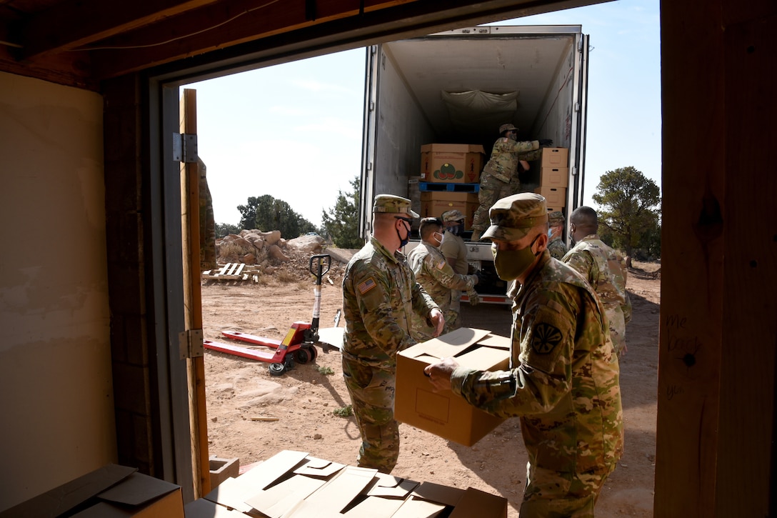 A group of male national guardsmen wearing face masks unload boxes from a truck.