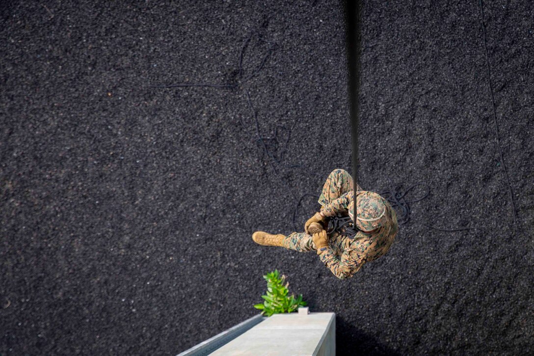 A Marine suspends from a rope above the ground.