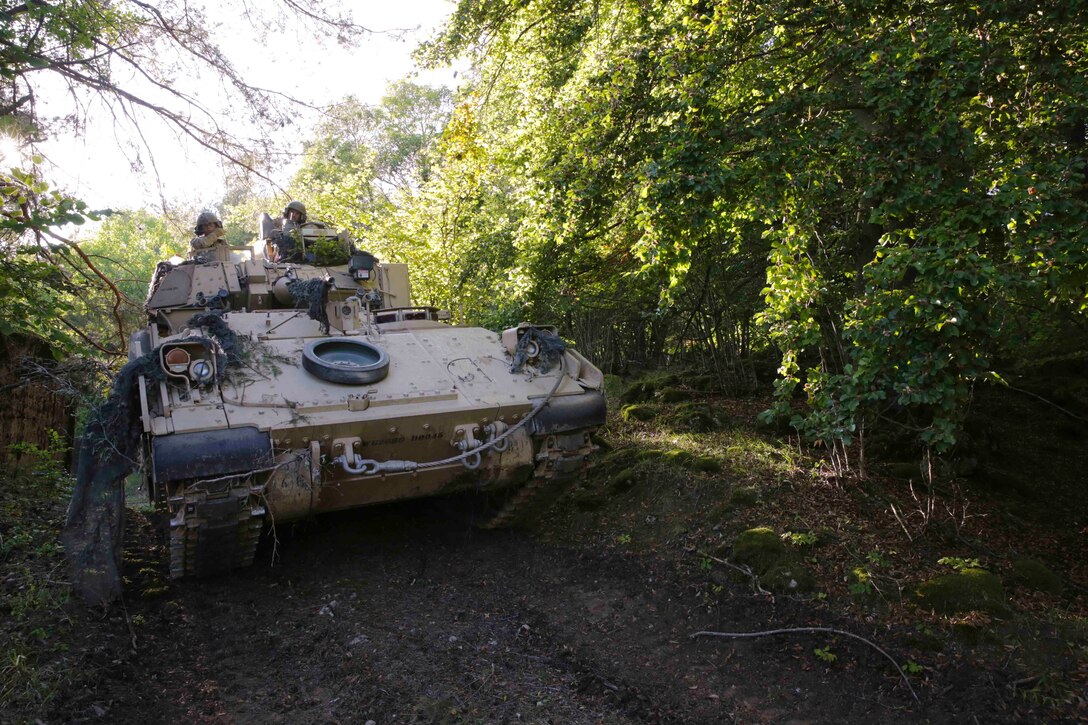 Soldiers travel in a military vehicle through trees.