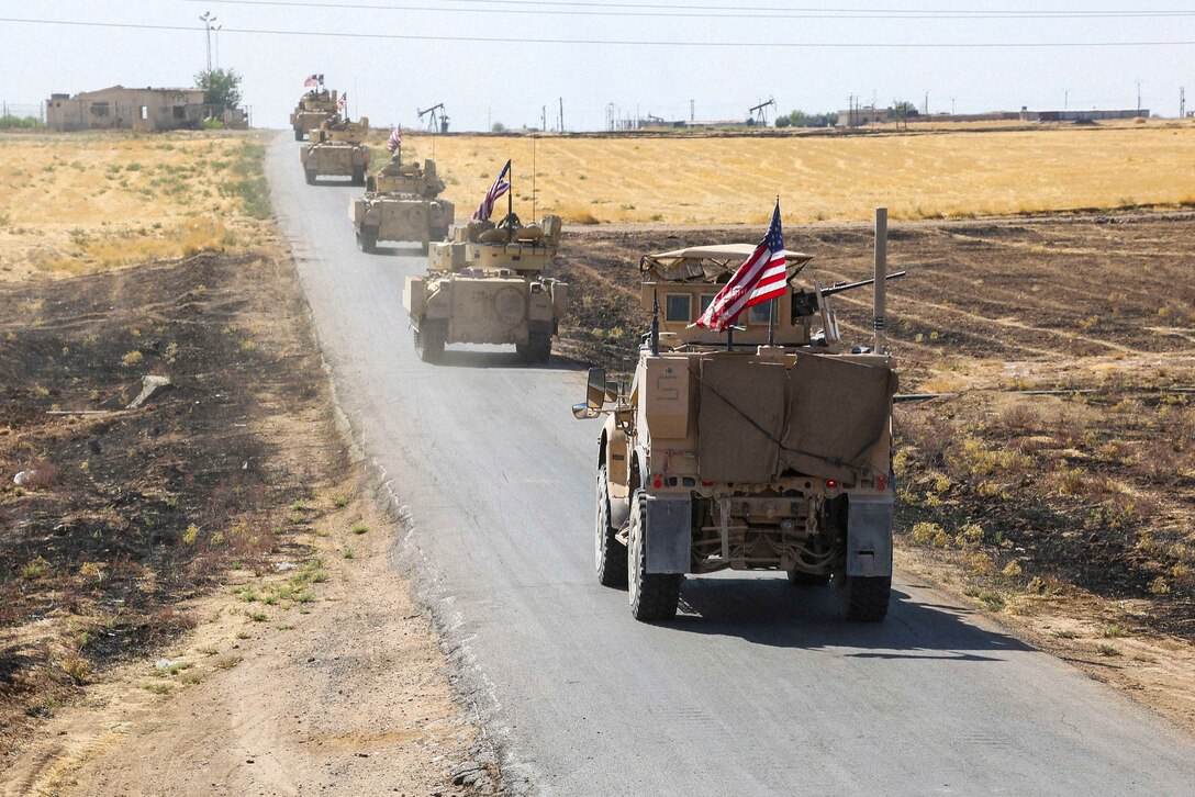 Five military vehicles travel down a road.