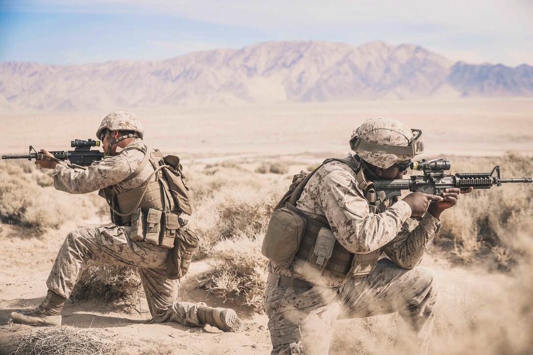 Two Marines kneel back-to-back while holding up their weapons.