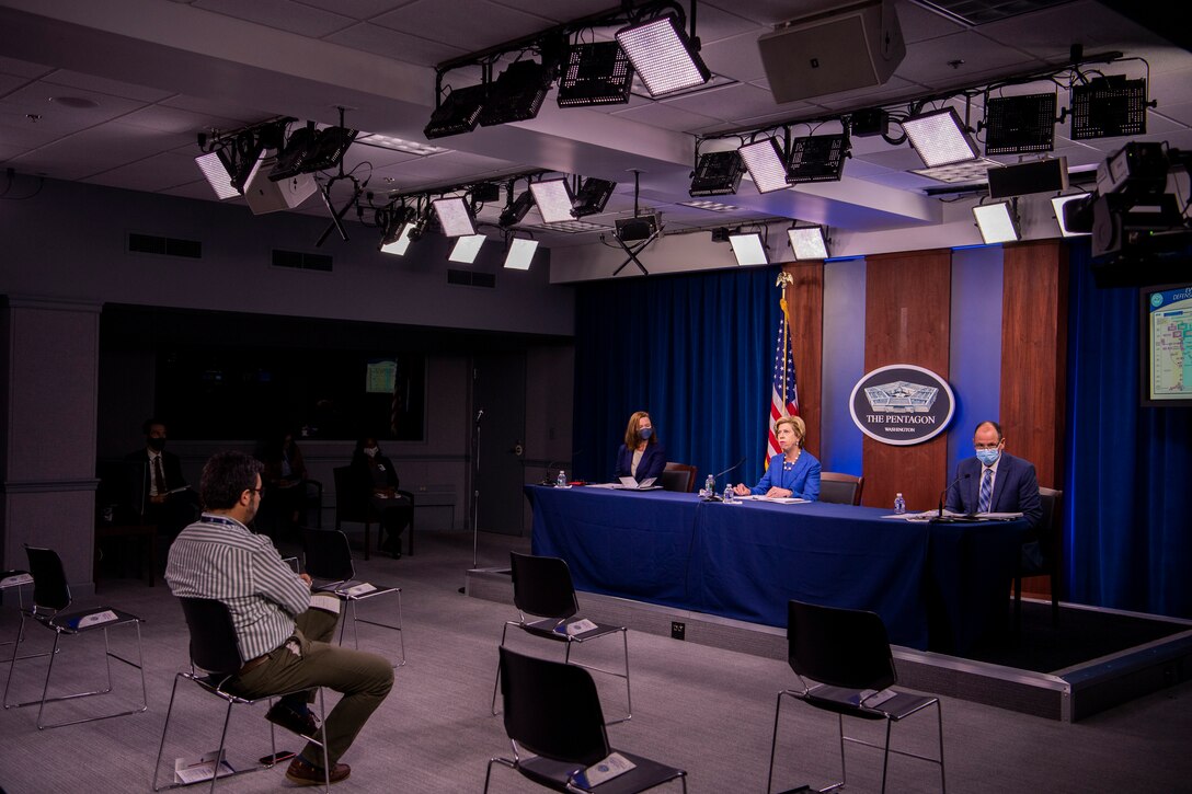 A woman, seated at a table, speaks into a microphone. The sign behind her indicates that she is at the Pentagon.