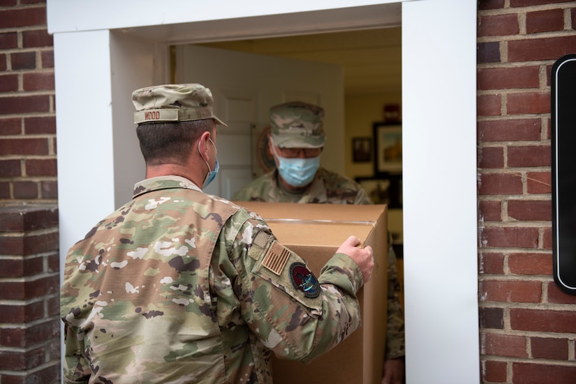 Two airmen wearing face masks carry a box.