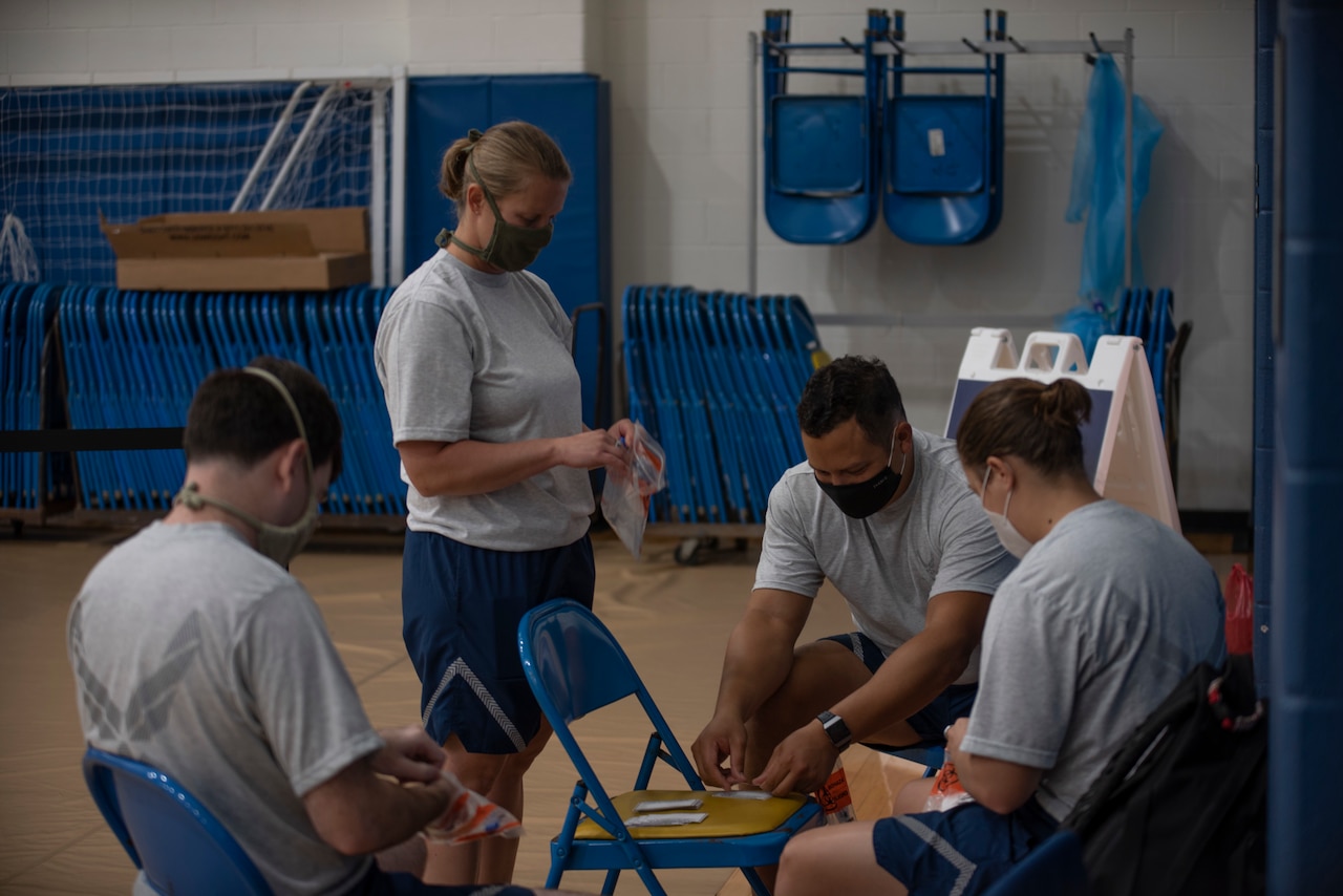 Airmen wearing face masks sit in a circle preparing COVID-19 nasal swab test kits.