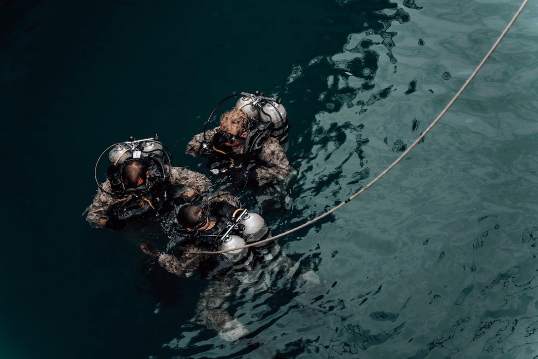 Three Marines wear diving gear in the water.