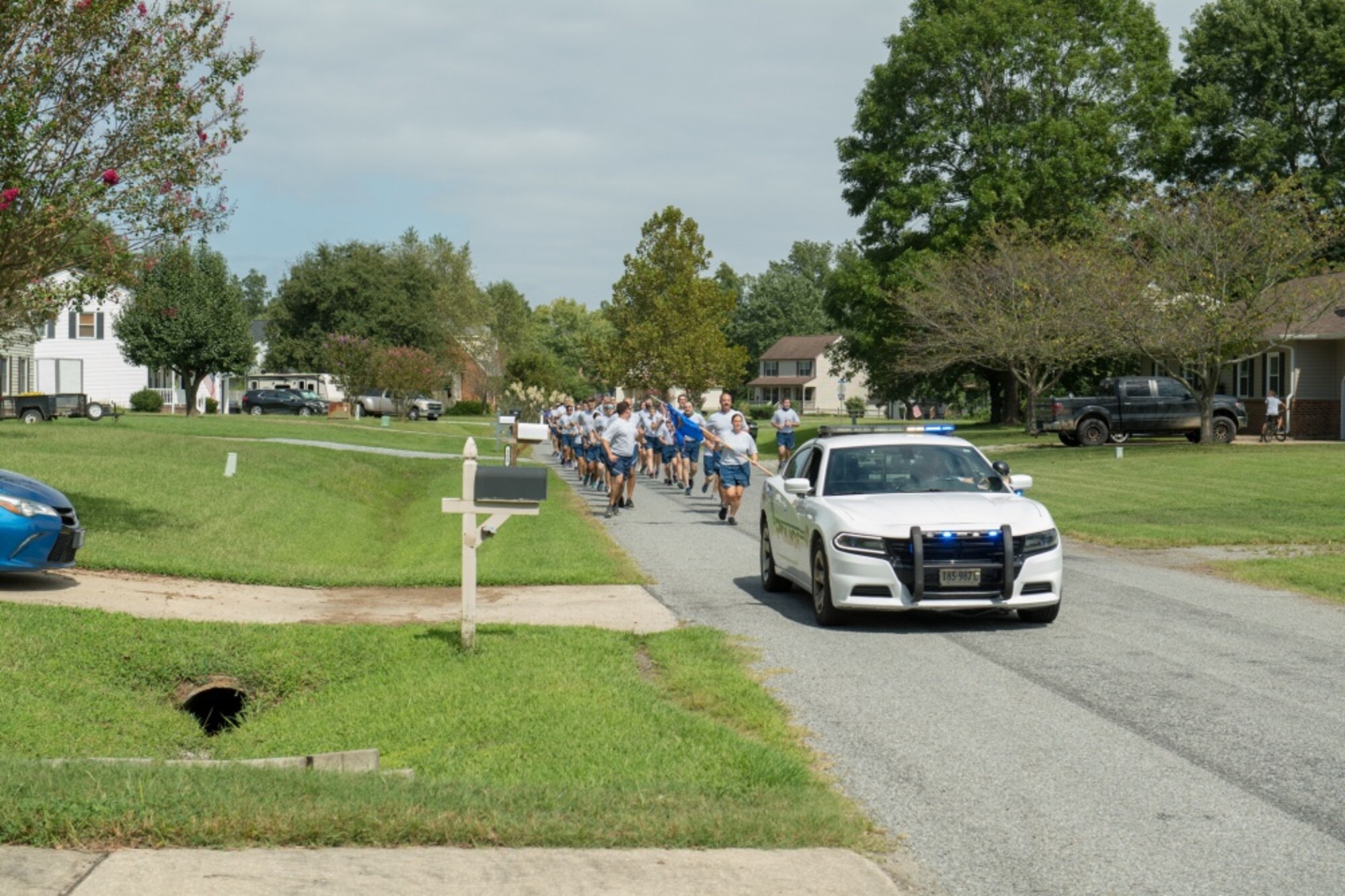 A law enforcement patrol vehicle escorts Airmen as they run through a neighborhood