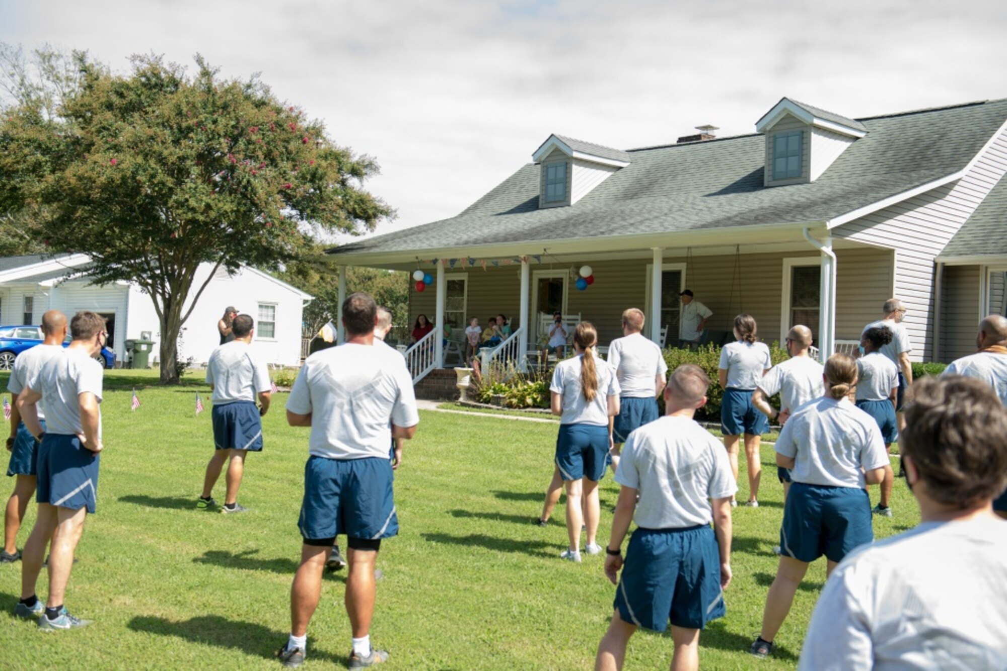 Airmen wearing their physical fitness uniforms stand facing a home