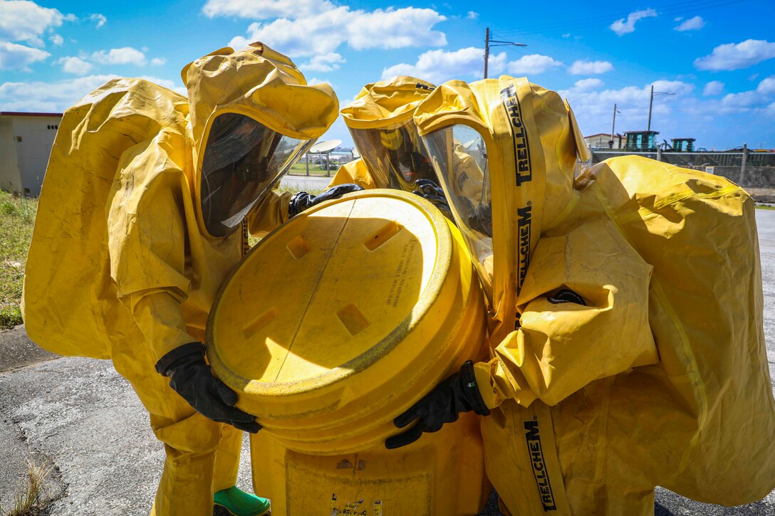 Three Marines in yellow personal protective equipment close a large plastic container.
