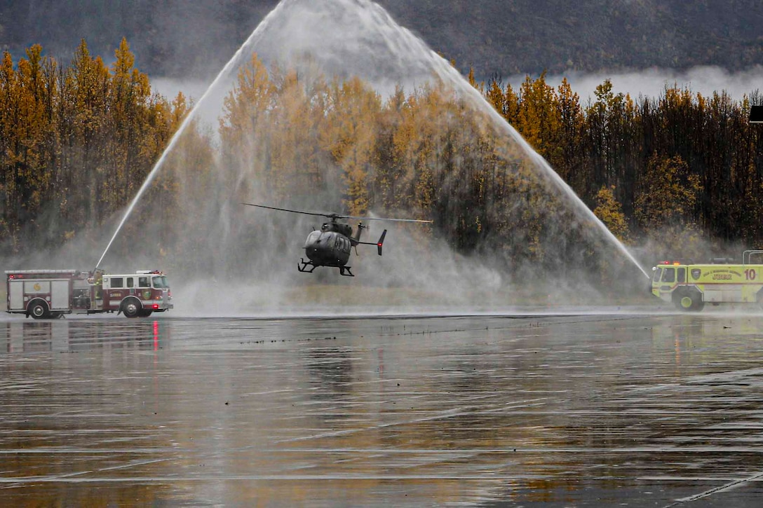 A helicopter flies underneath a spray of water from two firetrucks on either side.
