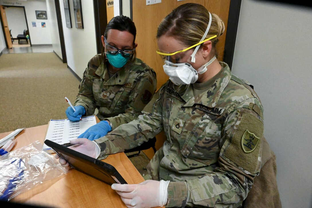 An airman and soldier sit at a table and look at a tablet.