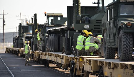 U.S. Army Soldiers secure military vehicles to rail cars.