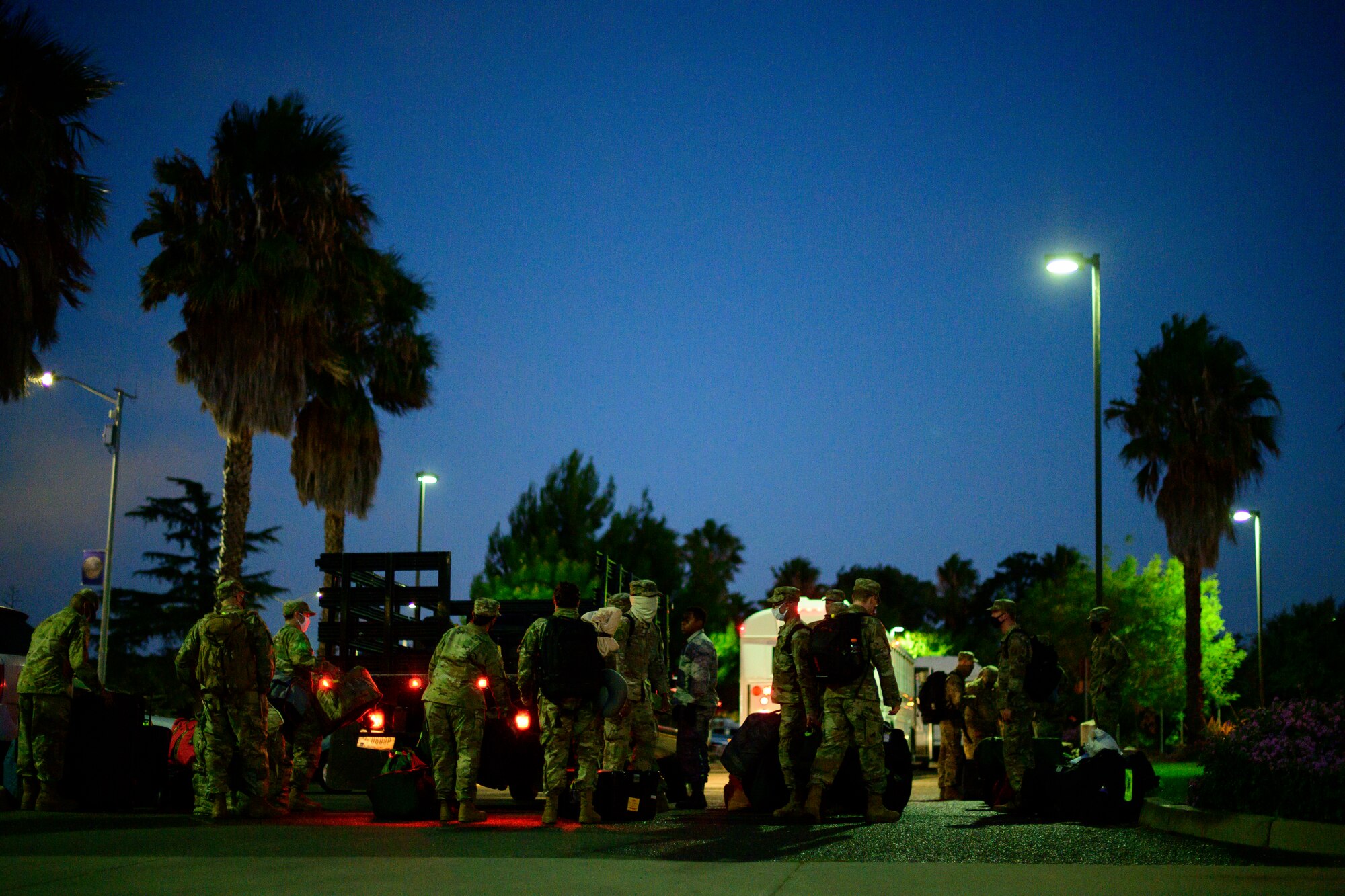 A very large group of Airmen stand in a line to place their bags in the back of a truck.