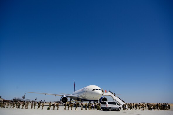 Men and women in military uniforms and face masks wait in a line inside airport-like surroundings