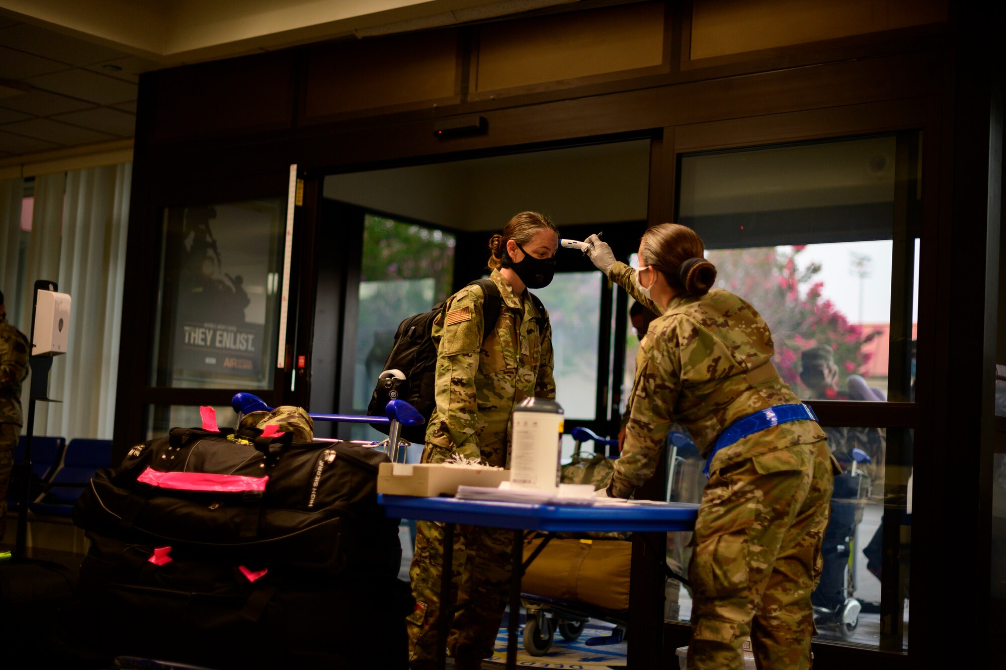 A female Airman takes the temperature of another female Airman inside a passenger terminal.