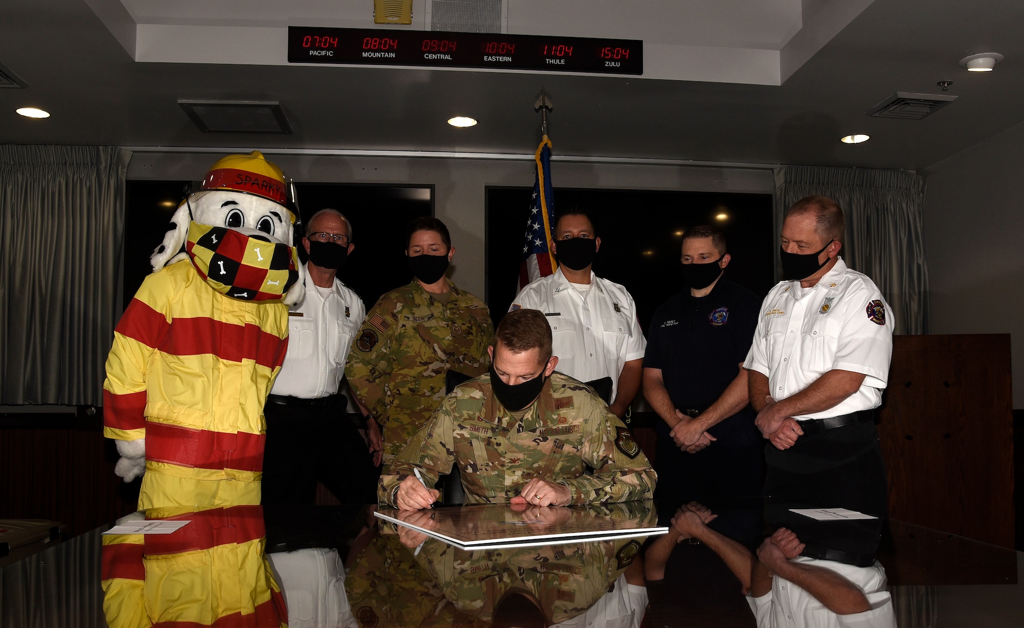 Picture of Col. Smith signing the proclamation while Sparky the Fire Dog and other fire department personnel stand behind him