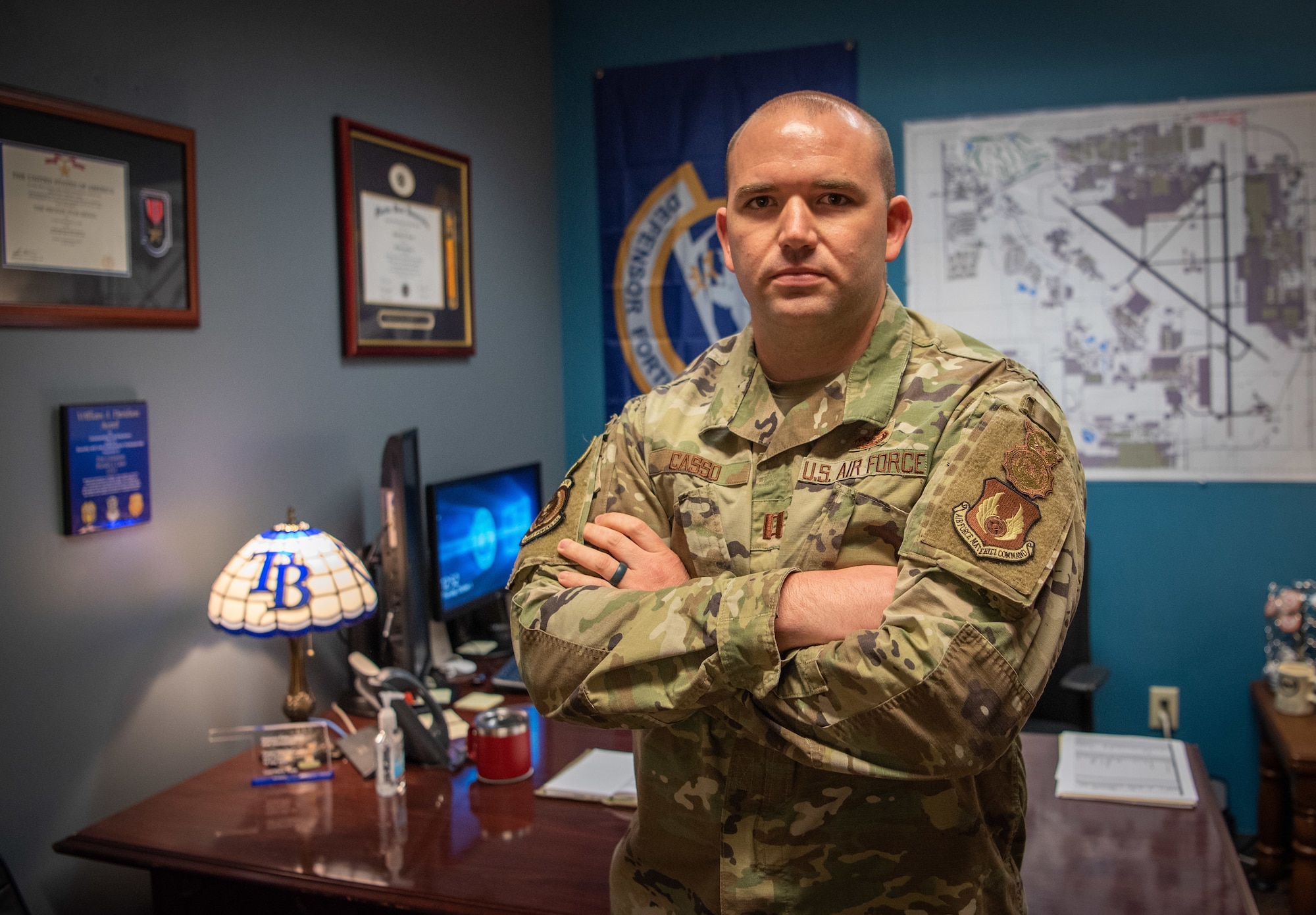 Airman with arms crossed standing in front of his desk.