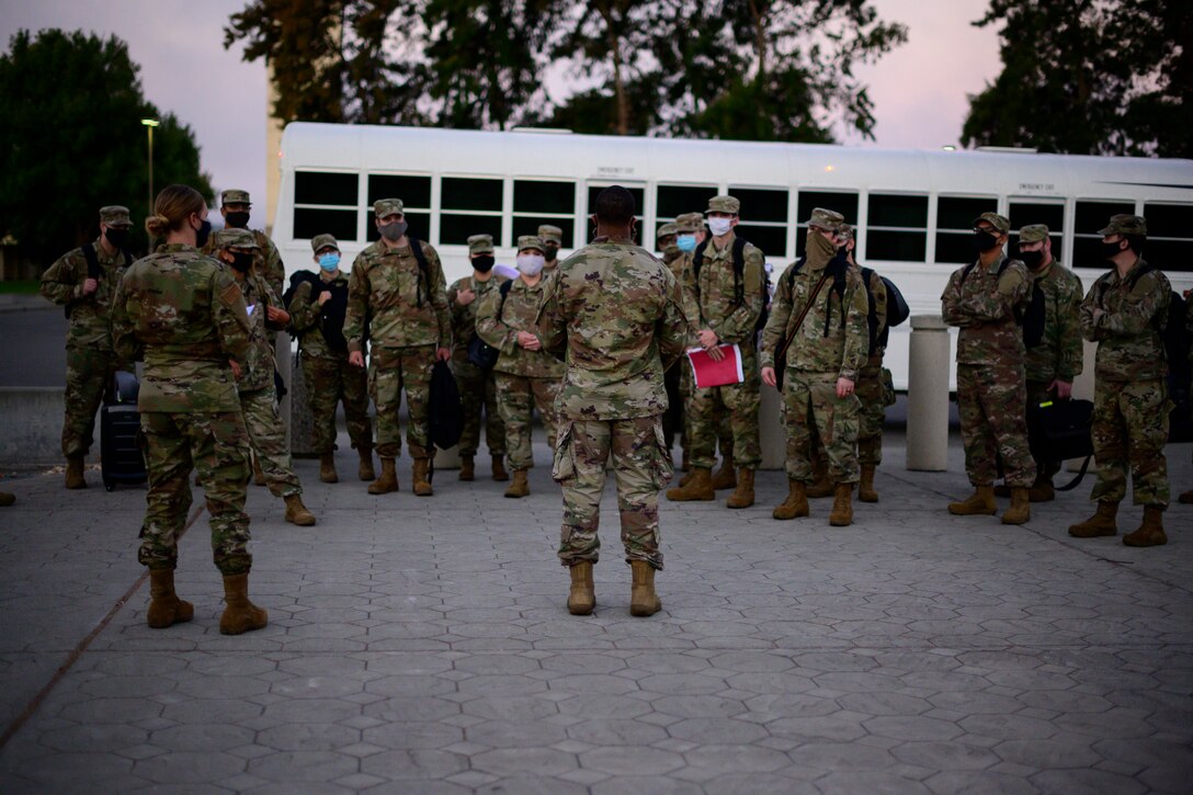 An Airman gives instructions to a group of Airmen standing in front of a large white bus.