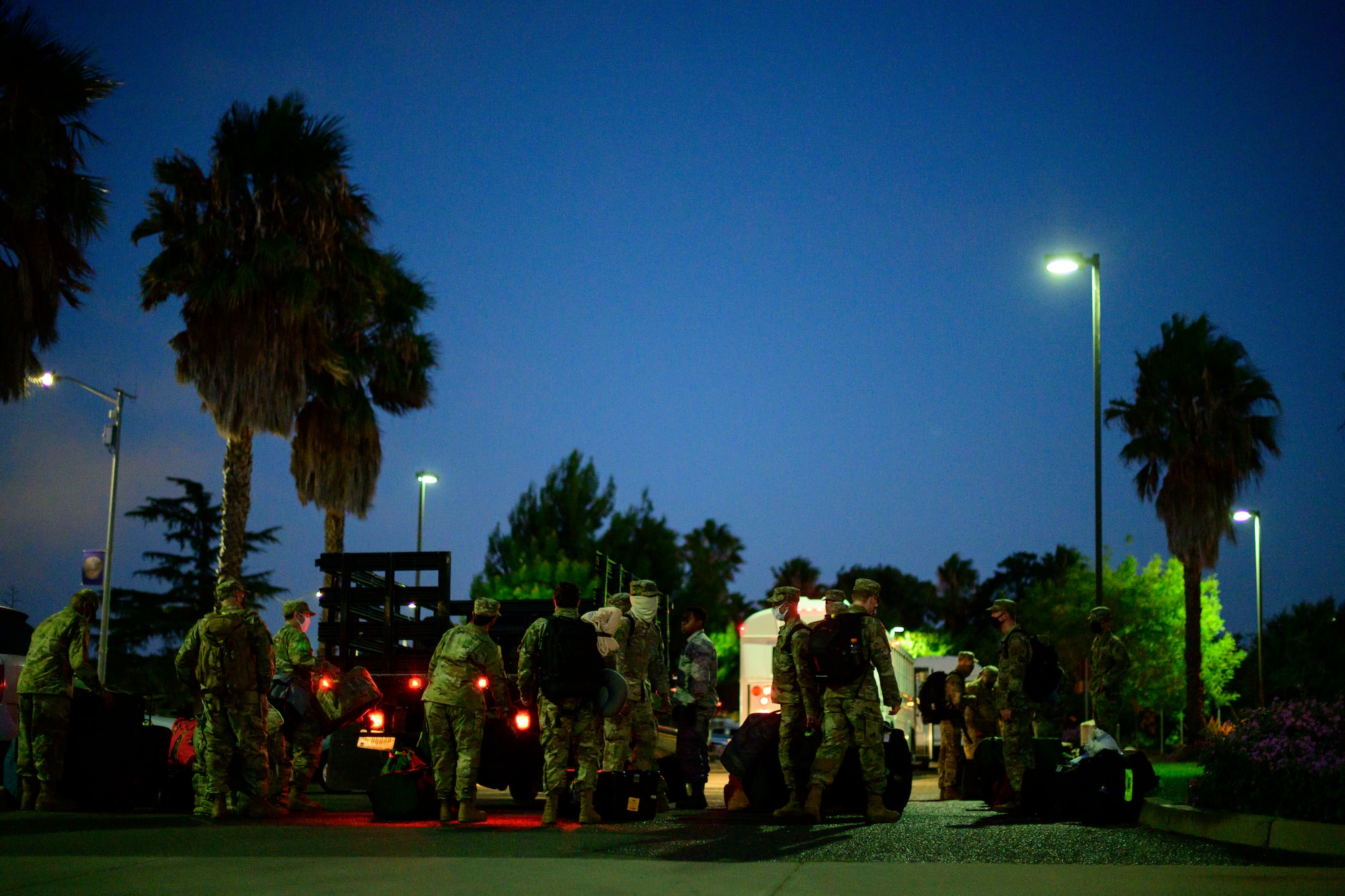 A very large group of Airmen stand in a line to place their bags in the back of a truck.