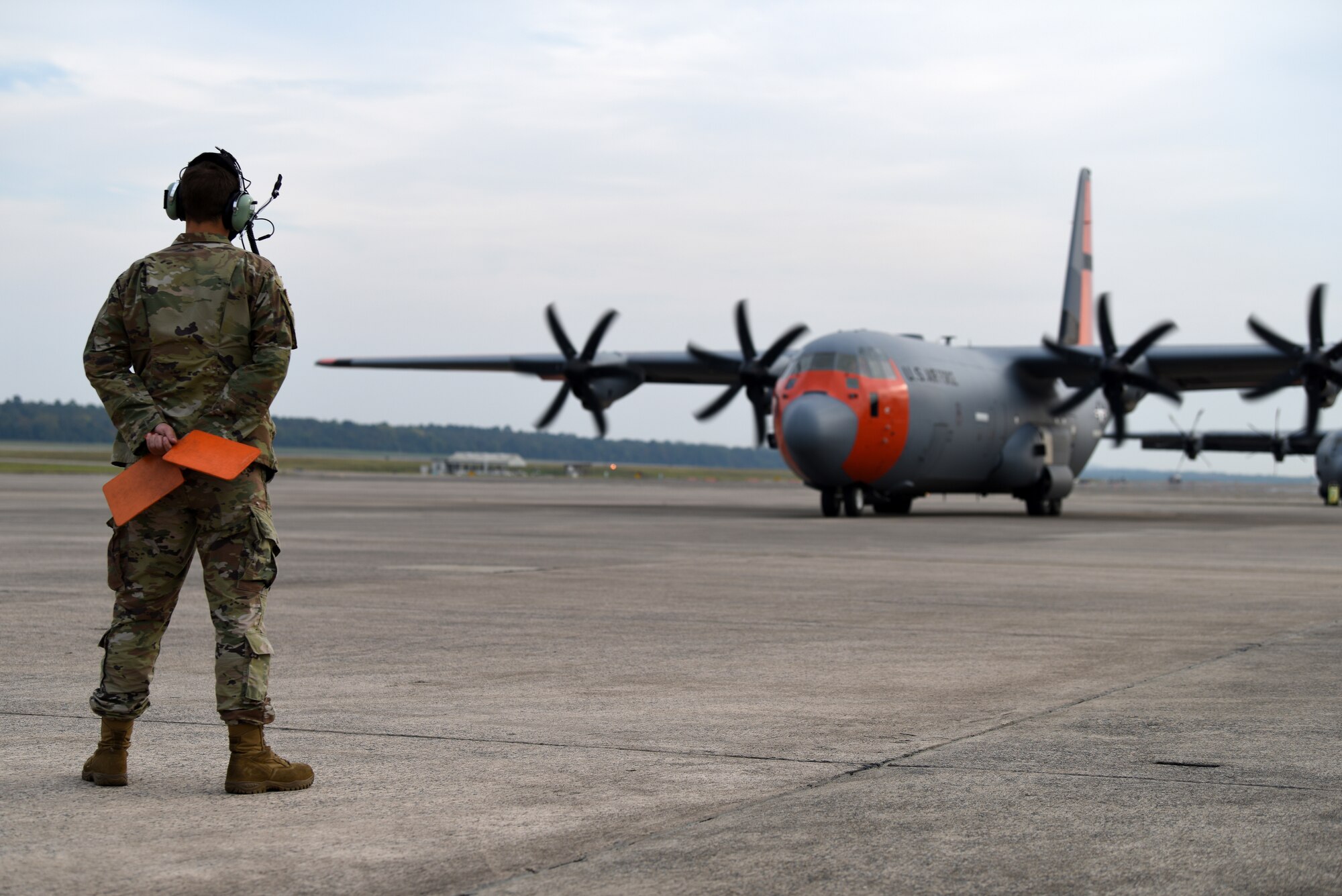Airman stands with marshaling flags behind back ready to direct plane