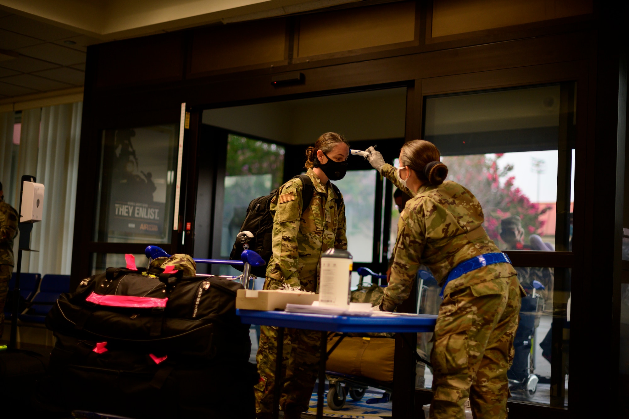 A female Airman takes the temperature of another female Airman inside a passenger terminal.