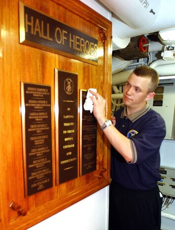 Mess Specialist Seaman Len Edwards puts the finishing touches on a large brass plaque, bearing the names of each Sailor killed in the October 12, 2000, terrorist attack, while the ship was refueling in the port city of Aden, Yemen.