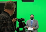 A customer account manager for DLA Disposition Services in Battle Creek, Michigan sits in front of a green screen in a TV studio.