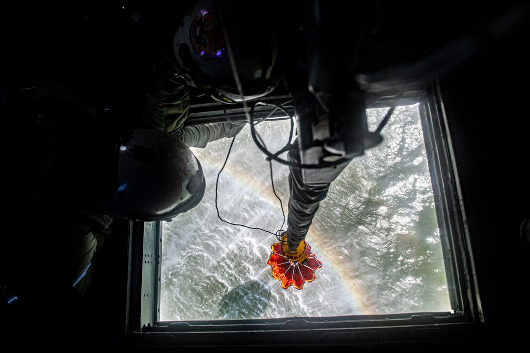 A sailor looks down from a helicopter at a bambi bucket above the water.