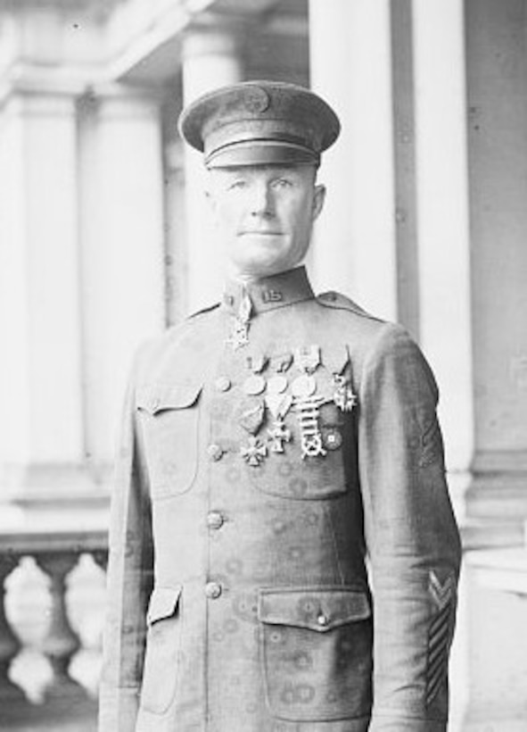 A man in military uniform stands amid pillars.