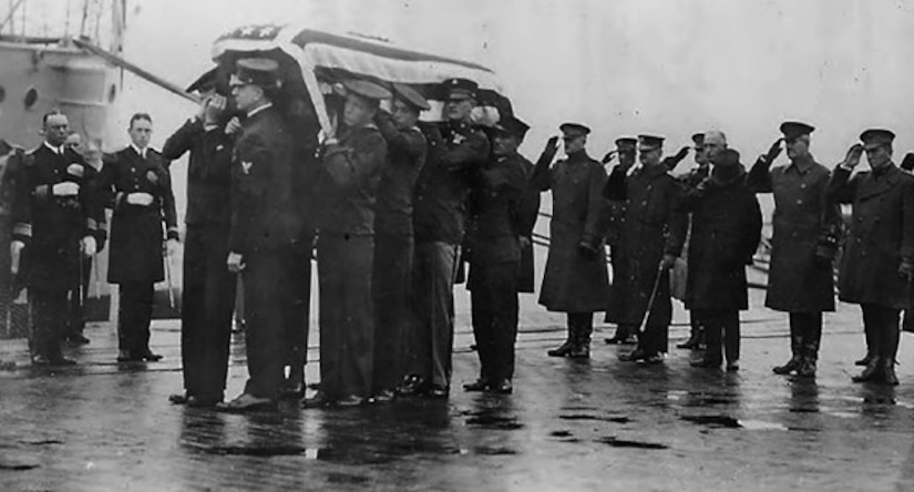 Several men salute as others carry a casket draped in an American flag.