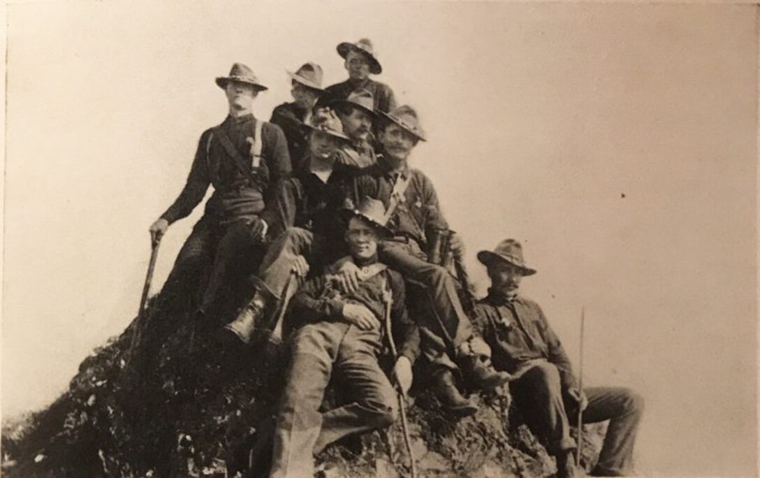 Eight men sit together on the top of a dirt mound.