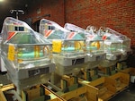 Five infant hospital beds are packaged in a warehouse awaiting delivery.