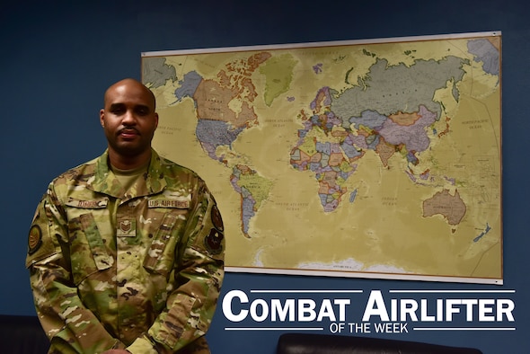 An Airman poses for a photo in front of a map.