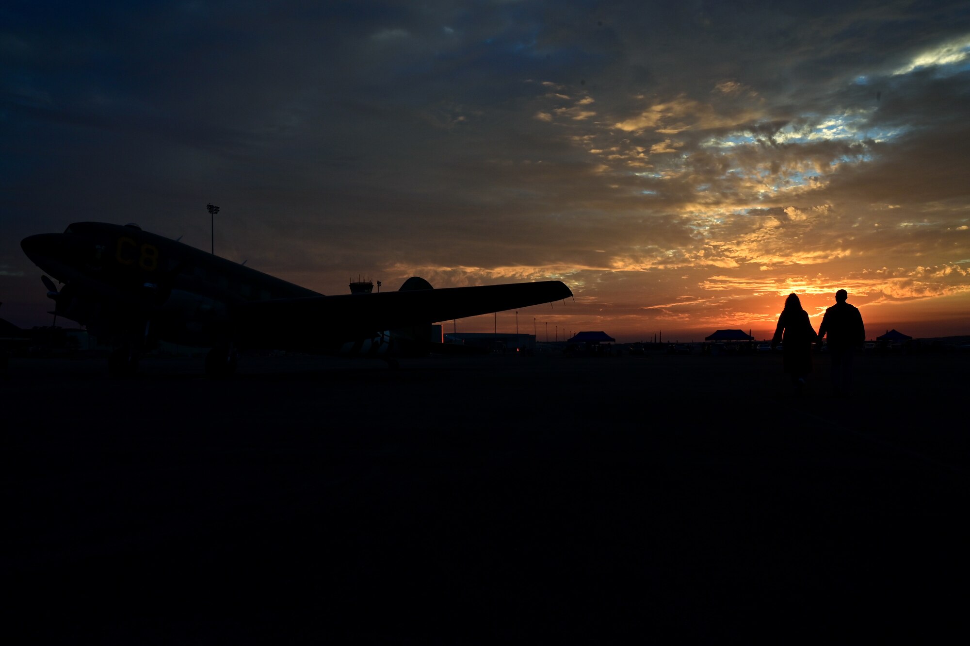 A couple walks behind a heritage Aircraft at sunset