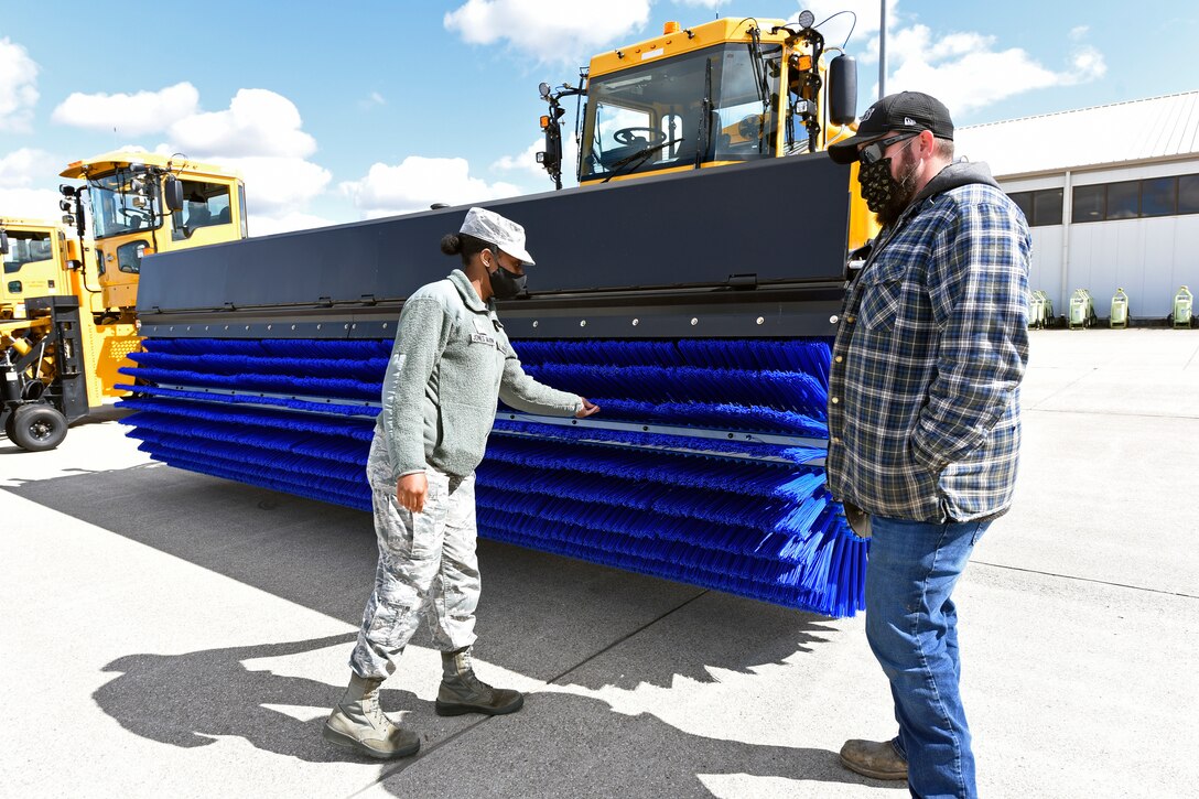 U.S. Air Force Senior Airman Royalty Jones-Gavin, command support, 88th Air Base Wing, inspects an Oshkosh airfield snow broom with heavy equipment operator Dustin McIver, 88th Air Base Wing Civil Engineer Group, before test driving the big machine at Wright-Patterson Air Force Base on Oct. 2, 2020. CEG drivers paraded the snow removal equipment across the airfield for review by 88 ABW Commander Col. Patrick Miller and local news reporters to demonstrate the equipment needed to keep the base and the airfield operational. (U.S. Air Force photo by Ty Greenlees)