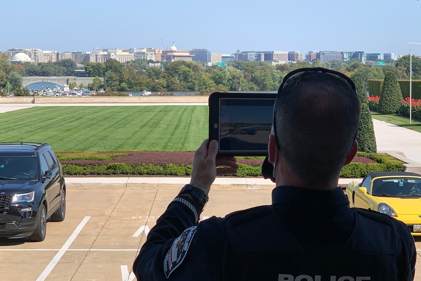 A Pentagon Force Protection Agency officer holds up a tablet while standing with a view of the Washington, D.C., skyline.