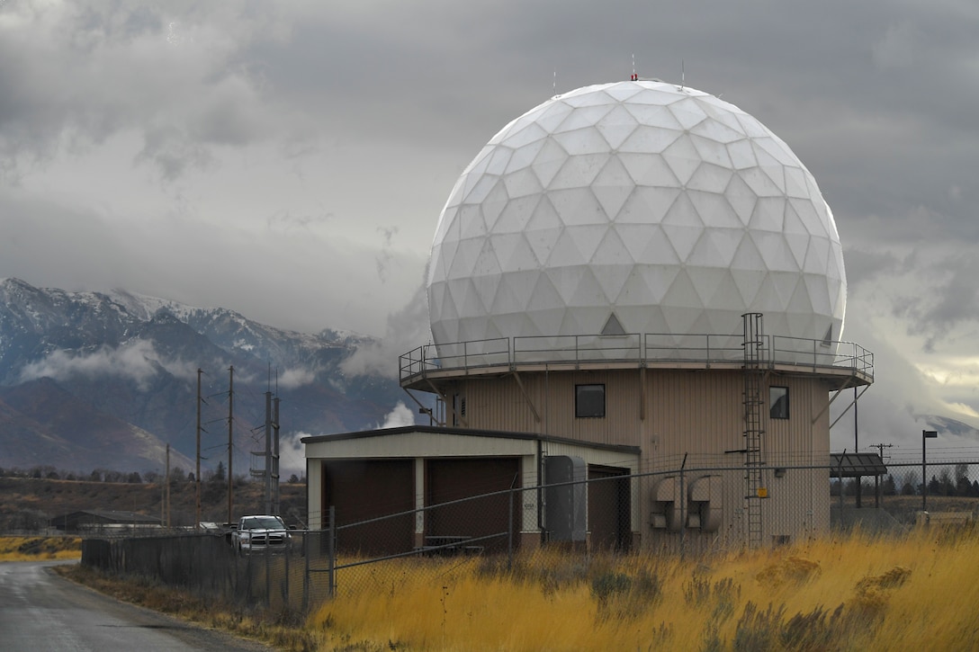 A golf ball-shaped building sits inside a fenced area with mountains in the background.