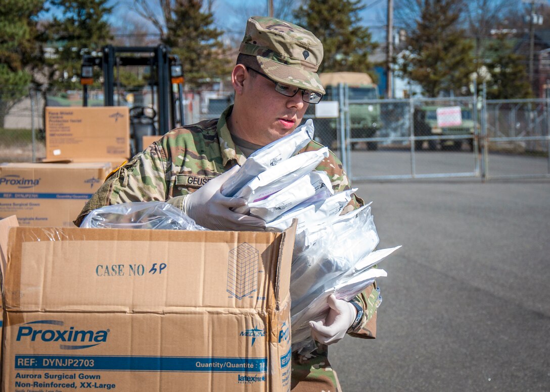A soldier holds packages of protective equipment that came from boxes in the foreground