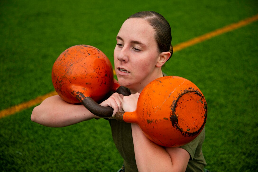 A Marine squats holding two kettlebells.