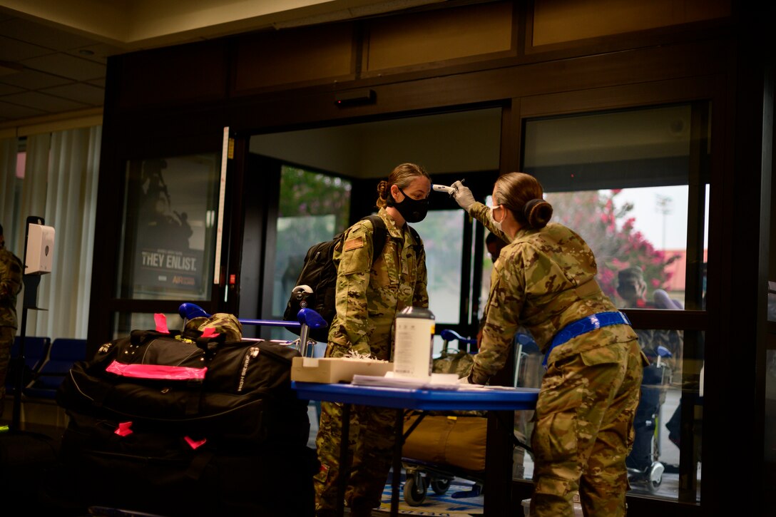 An airman wearing a face mask checks another airman's temperature.