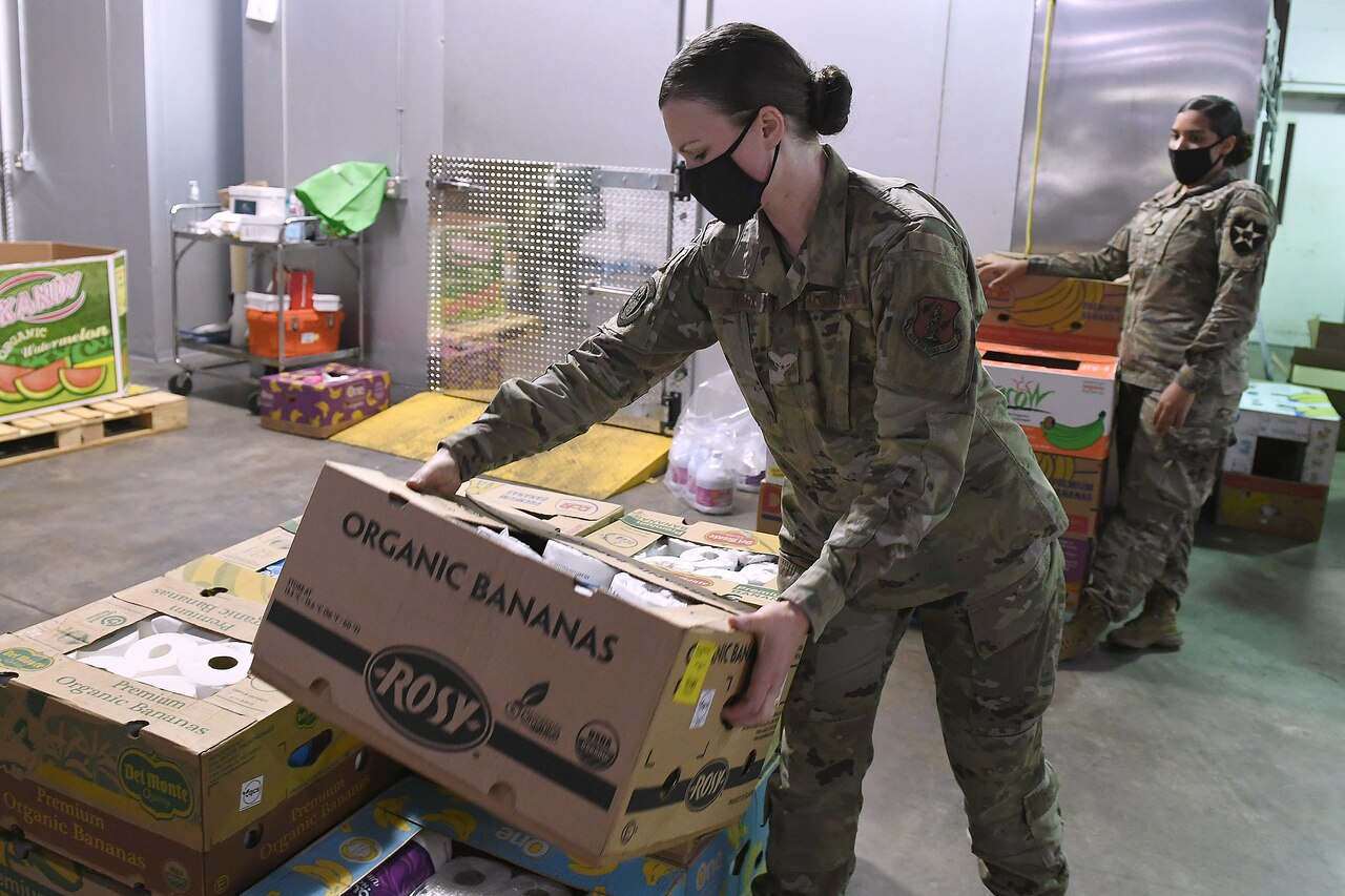 A female airman wearing a face mask lifts a box.