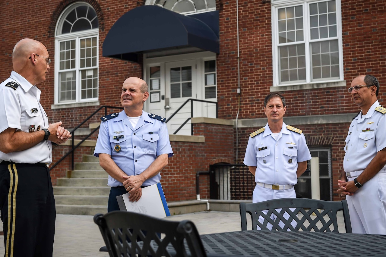 Four men wearing uniforms stand outside a building; two of the men are talking.