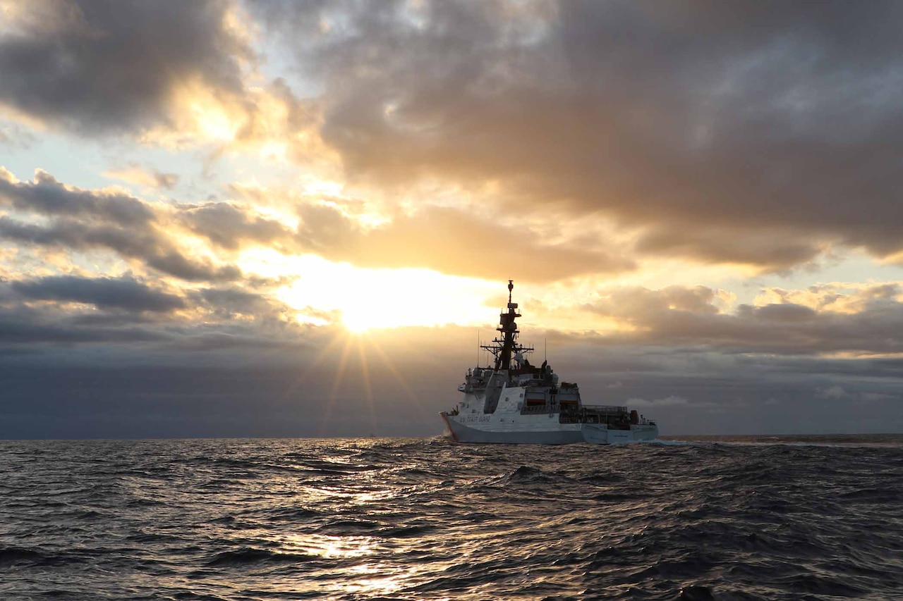 A ship sails on the ocean as the sun sets.