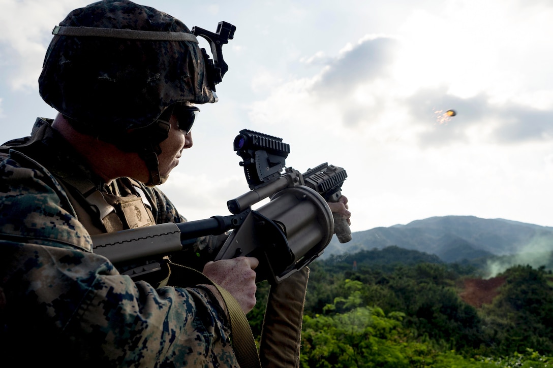 A Marines fires a grenade launcher in a forest-like area.