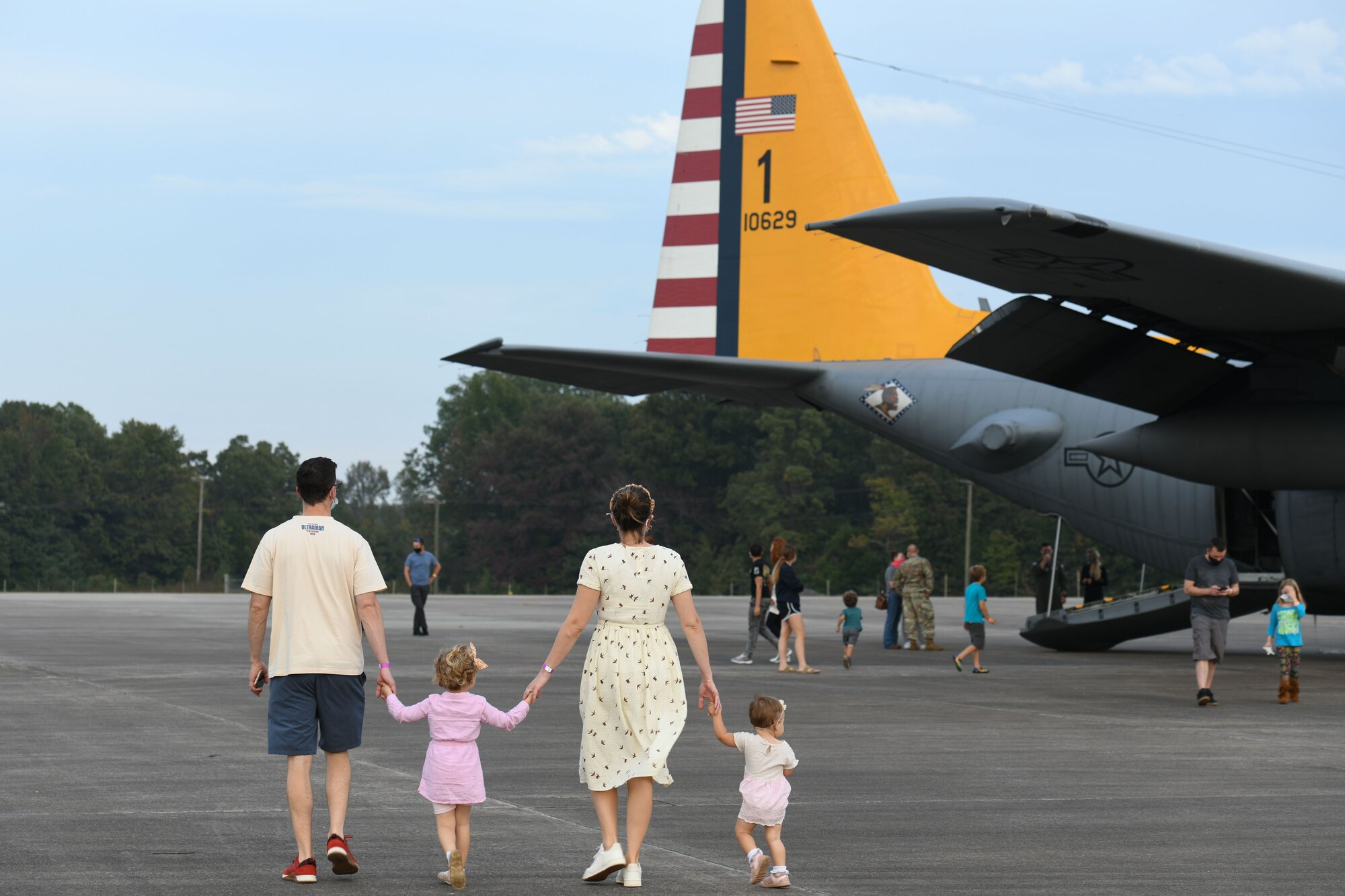 A Family of 4 walks holding hands towards a C-130 plane
