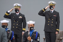Cmdr. Edward Pledger, commander, USS Cole (DDG 67) and Lt. j.g. Harry Hazell, Chaplin, USS Cole, salutes during the National Anthem at the Arleigh Burke-class guided missile destroyer USS Cole (DDG 67) 20th Anniversary memorial ceremony at Naval Station Norfolk.
