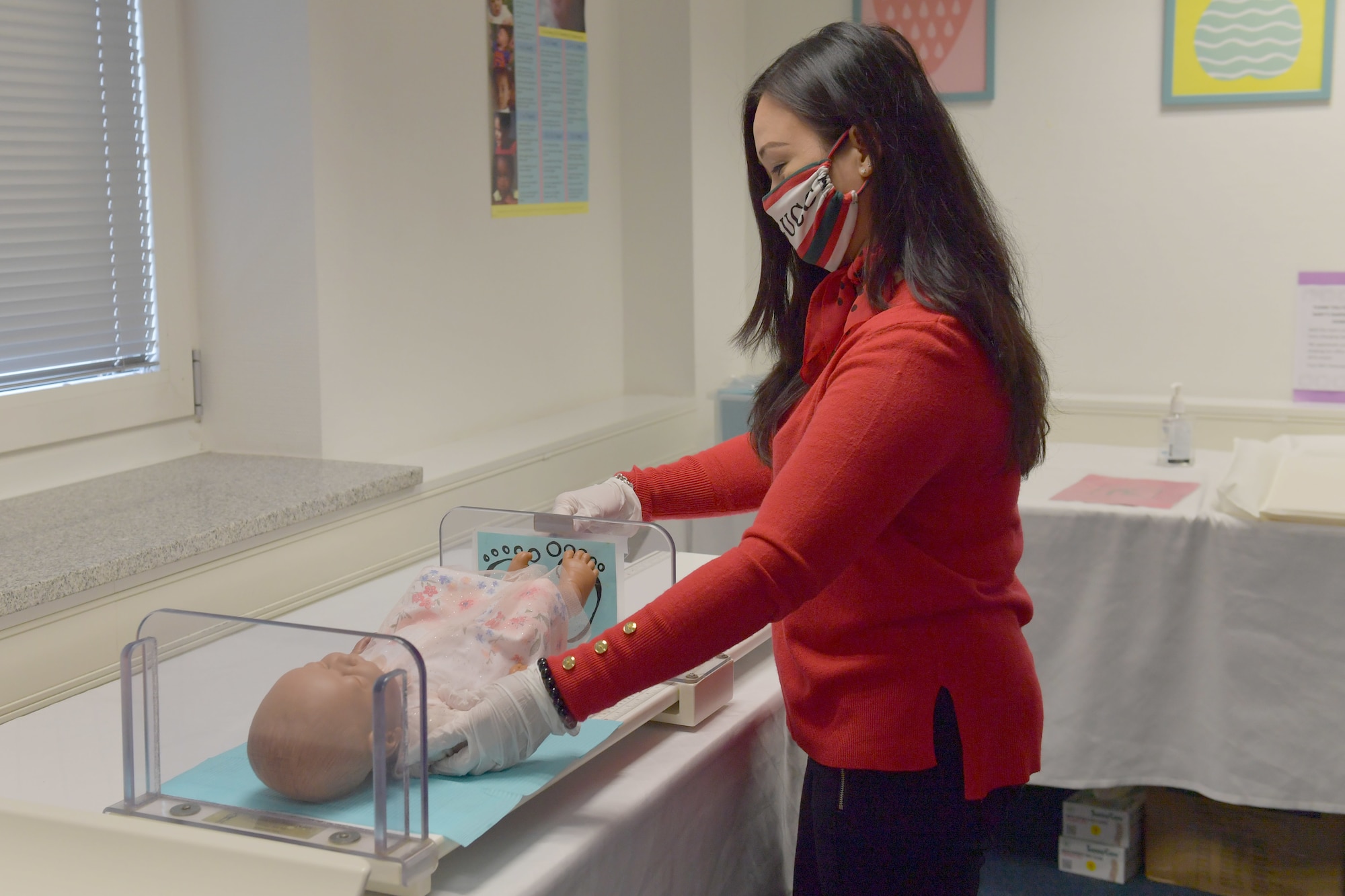 A woman measuring an infant mannequin.