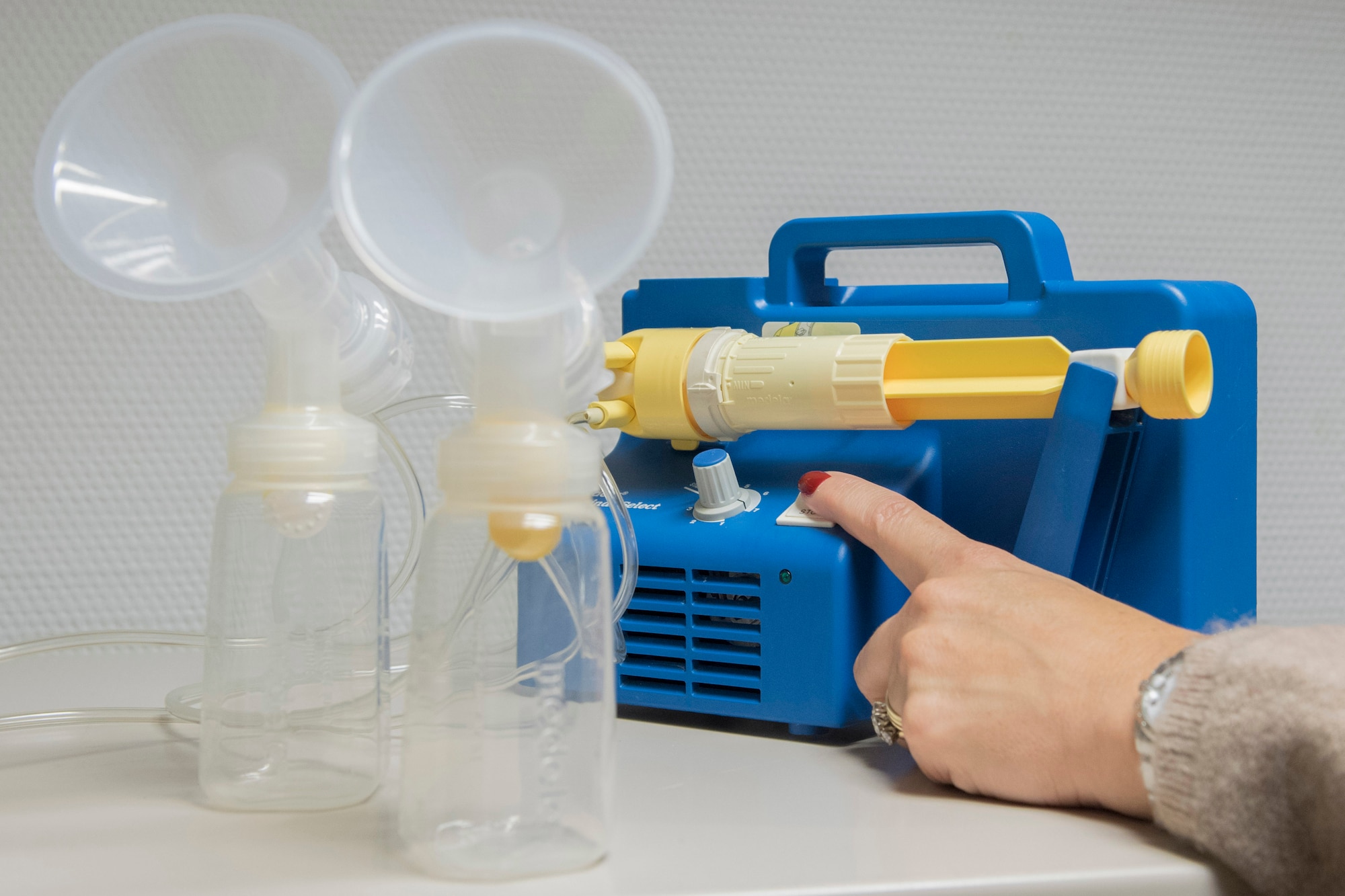 A hand pressing a button on a breast pump machine.